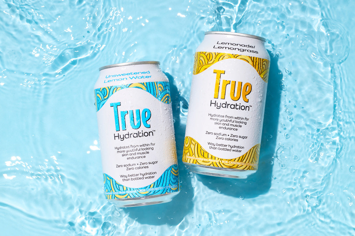 Two cans of True Hydration in shallow water on a blue background