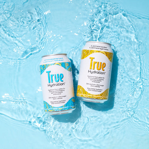 Two cans of True Hydration in shallow water on a blue background