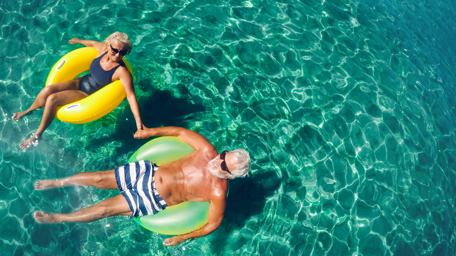 Older couple floating in a pool on a sunny day