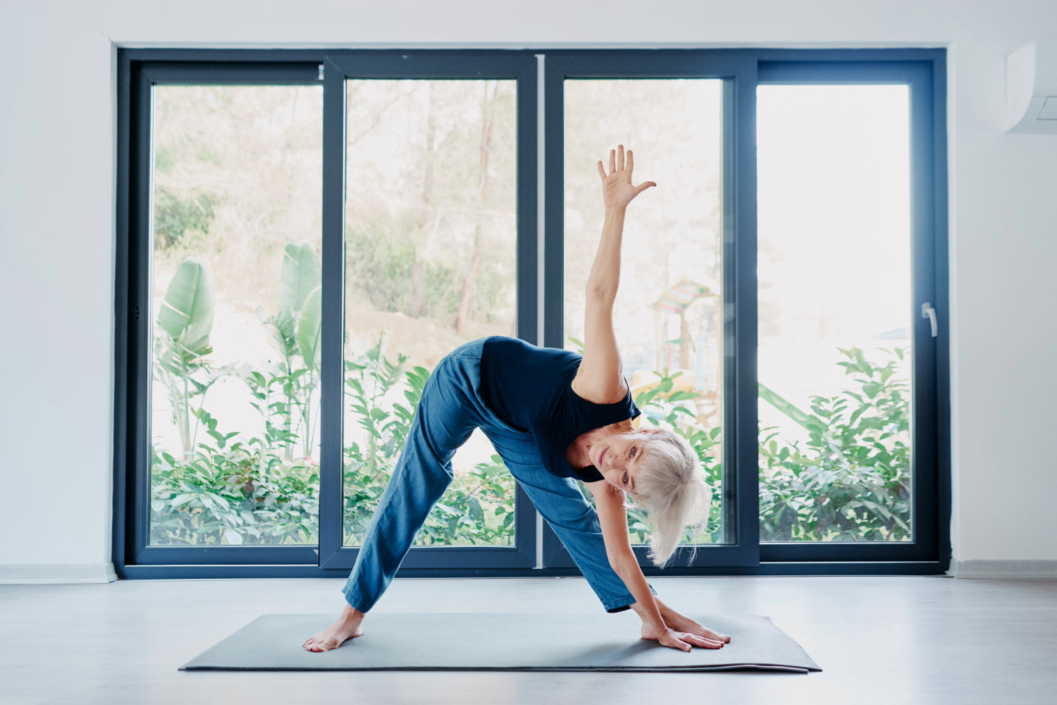 Middle age woman practicing yoga in front of large sunny window